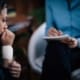 : A distressed woman with a bandaged wrist sits in a therapy session, speaking with a counselor who is taking notes.