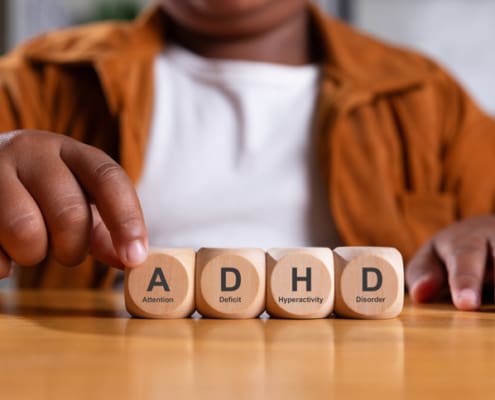 Hand Of Black Boy Puts Wooden Cube With ADHD.