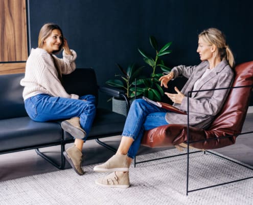 A Smiling Woman Listens To The Advice Of A Consultant Psychologist Sitting On A Sofa In The Workshop