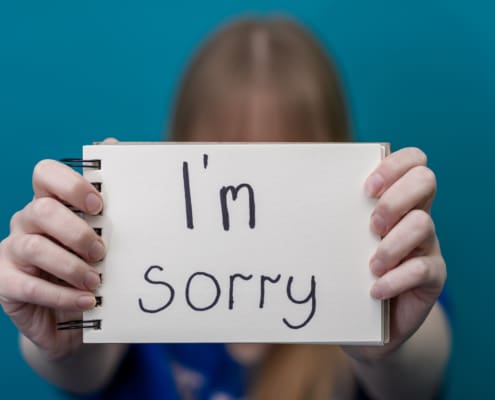 A Woman Holds A Card With The Words Sorry In Her Hands