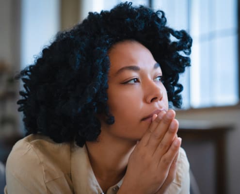 Discouraged Pensive African American Woman Looking Into Distance Thinking About Ways To Solve Financial Problems. Frightened Black Girl Sits On Sofa In Living Room Having Lost Mood Due To Inflation