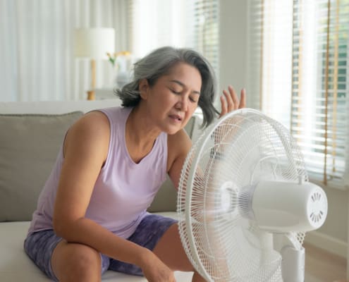 Asia Adult People Middle Age Old Woman Sit At Sofa Home Feel Hot Flash Fever Use Fan Waving Hand Blowing Wind Face Elder Health Care Summer Heat Aging Issue. Sad Pain Sweat Tired Stroke Suffer Stress.
