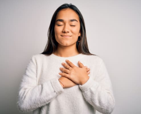 Young Beautiful Asian Woman Wearing Casual Sweater Standing Over White Background Smiling With Hands On Chest With Closed Eyes And Grateful Gesture On Face. Health Concept.
